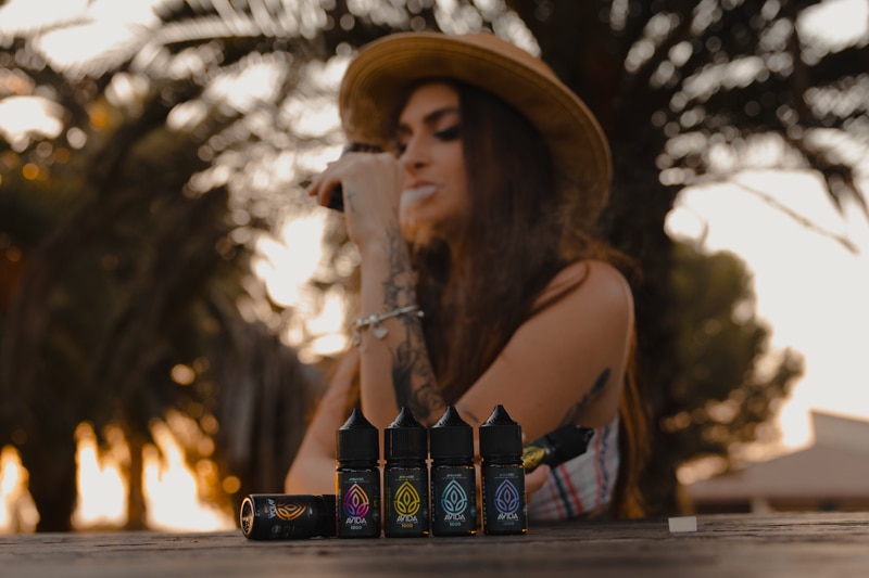 woman vaping cbd in nature sitting on a table with cbd vape juices