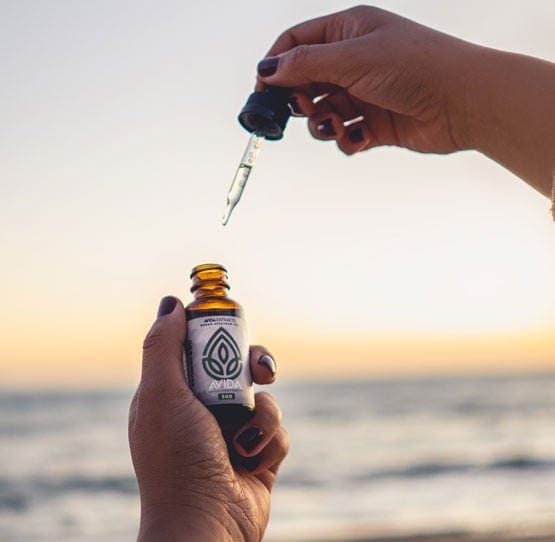 Broad Spectrum CBD oil Drops being used by a girl on a beach with a beautiful sunset.