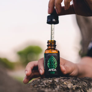 full spectrum cbd oil sitting on a rock with girl using dropper to pull CBD oil out of bottle. 