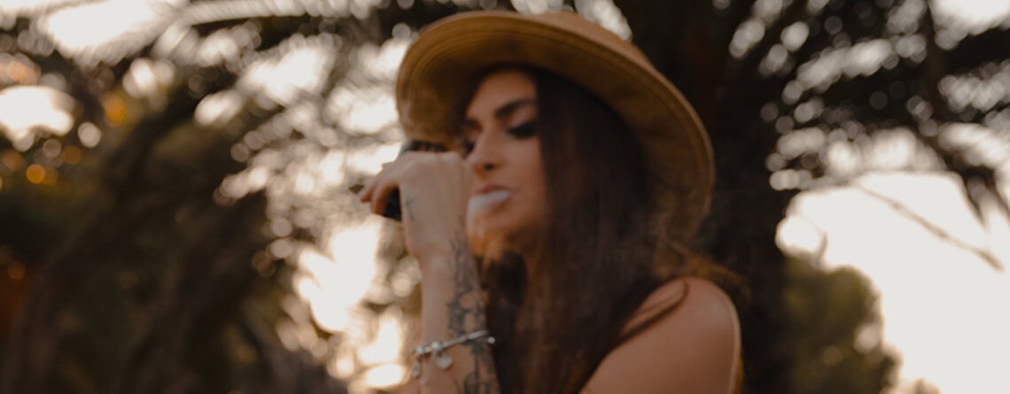 woman using a CBD vape pen on a park bench at sunset.