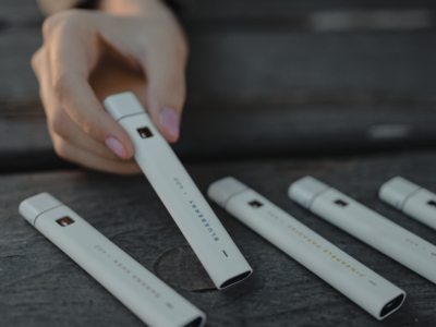 A hand holding a blueberry avida cbd 400 full spectrum cbd oil pen. 4 other flavors laying down on a wood plank.